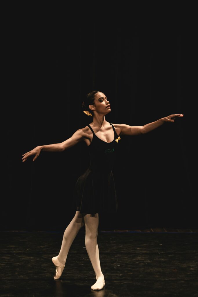 Graceful ballerina performing a ballet dance on stage under dramatic lighting.