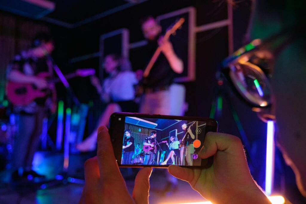 Close-up of a smartphone filming a live band performance in a vibrant setting.